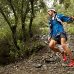 Мужчина в синей олимпийке и красных кедах бежит по пересеченной местности